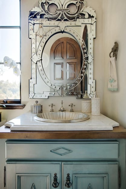 An upcycled vintage dresser transformed into a bathroom vanity. The dresser is painted in a muted teal colour, with a white ceramic sink and modern chrome faucet installed on top.