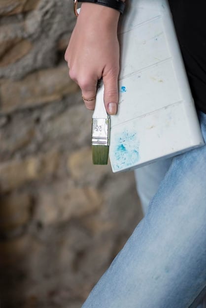 A close-up photo of a painter carefully applying primer to a section of exterior wall. The wall is made of wood and shows some minor imperfections. The painter is using a small brush to reach into corners and crevices.