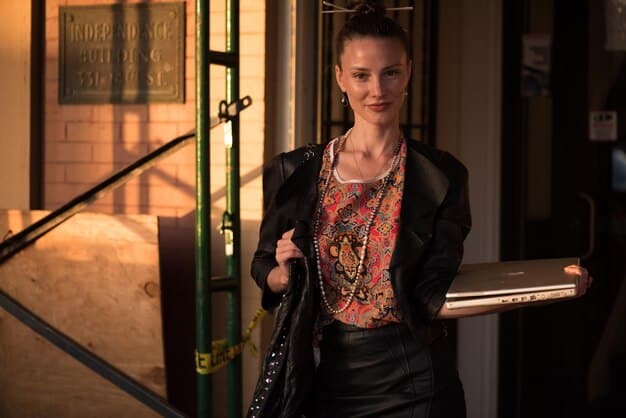 A woman in a bustling office environment wearing a bohemian blouse tucked into tailored trousers, accessorized with subtle jewelry.