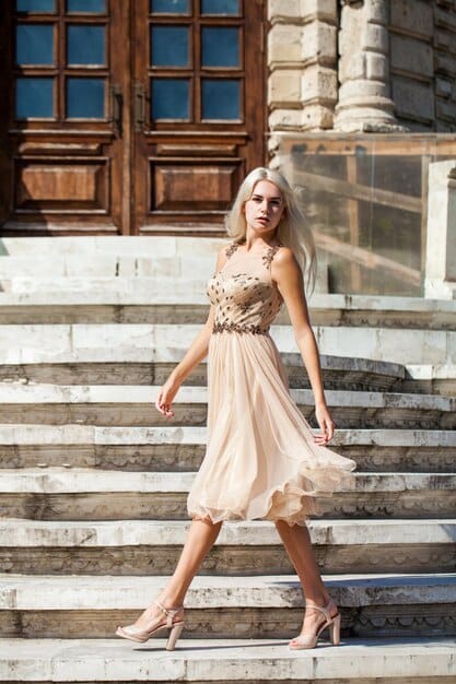 A stylish young woman dressed for an evening out, wearing a midi slip dress layered with an elegant oversized blazer, accessorized with delicate jewelry and heeled ankle boots, in a subtly lit urban setting.