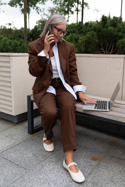 A professional woman in an office setting, wearing a tailored Tencel blazer, matching trousers, a recycled silk blend blouse, and classic recycled leather loafers.