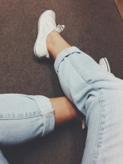 A close-up shot of trendy white chunky sneakers on a woman's feet, paired with distressed denim jeans and a simple white t-shirt, emphasizing casual comfort and modern style.
