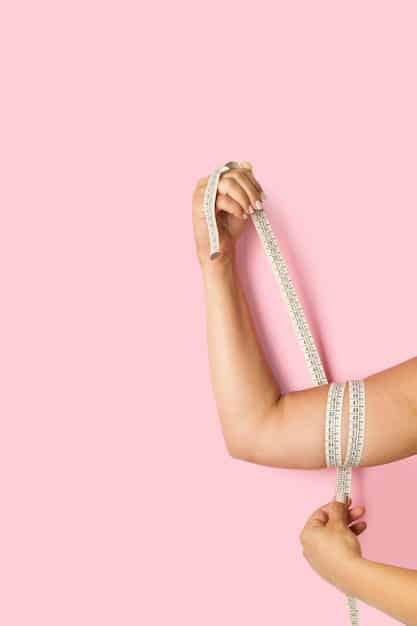 A close-up of a hand holding a measuring tape against a lace bra, illustrating the process of taking body measurements for lingerie. The background is softly blurred to keep focus on the measuring process.